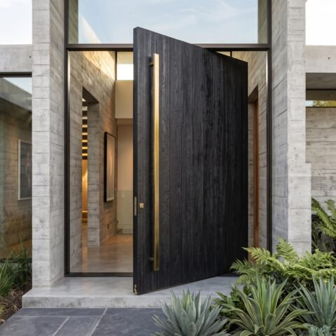 Modern black double heighted pivot door with oversized architectural entrance and concrete exterior