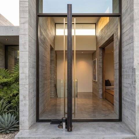 Modern black double heighted pivot door with oversized architectural entrance and concrete exterior