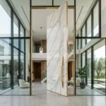 Double heighted white marble pivot door with gray veining, gold trim and vertical handle in a luxury modern interior