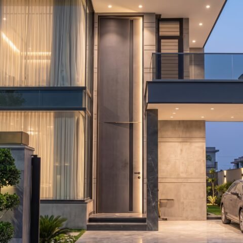 A towering matte grey double heighted pivot door with a vertical LED light strip installed in a luxury modern villa by Tarkhan Door.