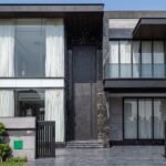 A massive matte black double heighted pivot door framed by black veined marble on a luxury modern residence by Tarkhan Door.