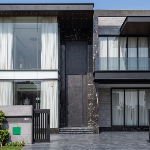 A massive matte black double heighted pivot door framed by black veined marble on a luxury modern residence by Tarkhan Door.