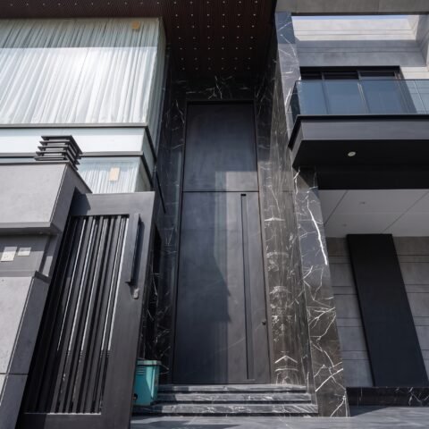 A massive matte black double heighted pivot door framed by black veined marble on a luxury modern residence by Tarkhan Door.