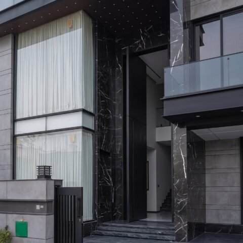 A massive matte black double heighted pivot door framed by black veined marble on a luxury modern residence by Tarkhan Door.